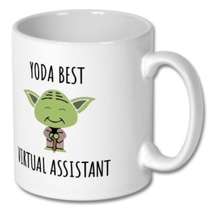 May include: White ceramic coffee mug featuring a green cartoon character of Yoda from Star Wars. The text "Yoda Best Virtual Assistant" is printed on the mug.