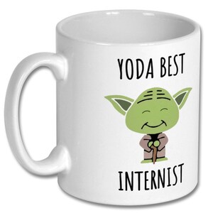 May include: White ceramic coffee mug with a green cartoon Yoda character holding a walking stick. The text "Yoda Best Internist" is printed on the mug.