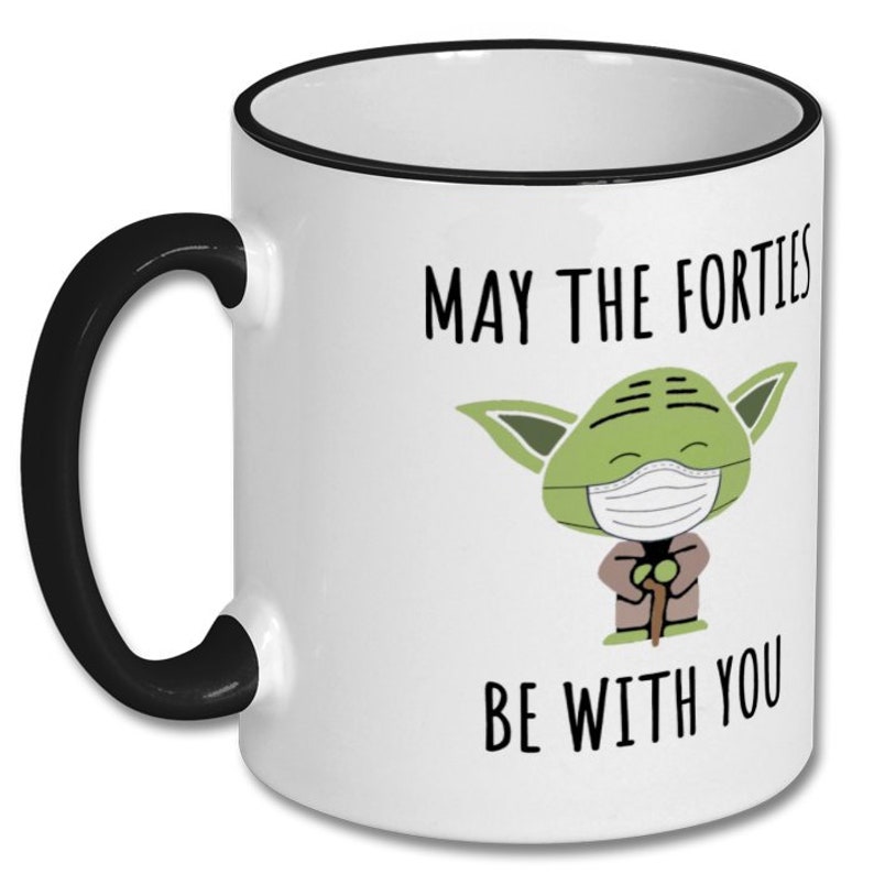May include: White ceramic coffee mug with a black rim and handle. The mug features a green cartoon character wearing a face mask and the text "May the Forties Be With You".