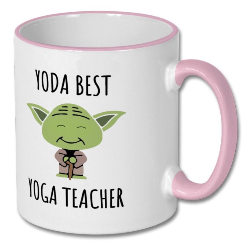 May include: White ceramic coffee mug with a pink rim and handle. The mug features a cartoon image of Yoda from Star Wars holding a walking stick and the text "Yoda Best Yoga Teacher".
