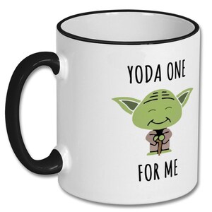 May include: White ceramic coffee mug with a black rim and handle. The mug has a green cartoon character with the text "YODA ONE FOR ME" printed on it.
