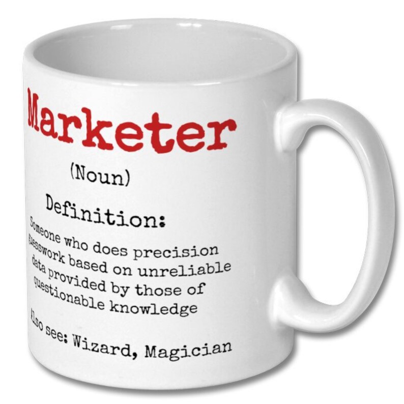 May include: White ceramic coffee mug with a red and black graphic that says "Marketer (Noun) Definition: Someone who does precision work based on unreliable data provided by those of questionable knowledge Also see: Wizard, Magician"