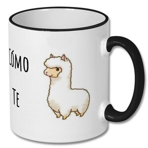 May include: White ceramic coffee mug with a black rim and handle. The mug features a cartoon illustration of a white llama with black eyes and a black nose. The text "COMO TE" is printed in black on the mug.