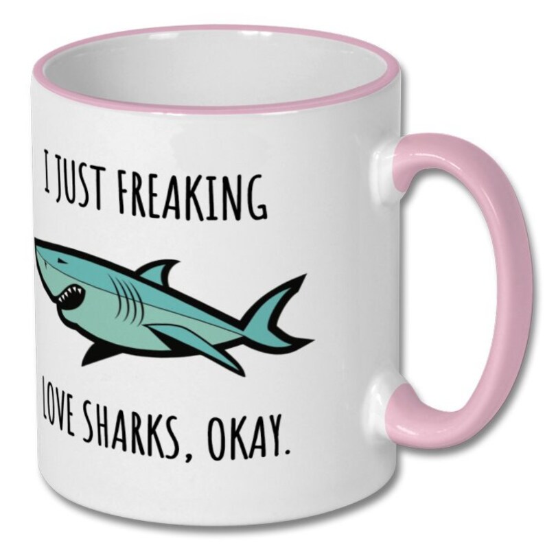Puede incluir: Taza de caf&eacute; de cer&aacute;mica blanca con borde y asa de color rosa. La taza presenta un tibur&oacute;n de dibujos animados y el texto "Me encantan los tiburones, &iquest;vale?"