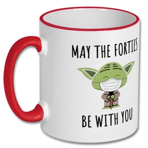 May include: White ceramic coffee mug with a red rim and handle. The mug features a green cartoon character wearing a face mask and the text "May the Forties Be With You".
