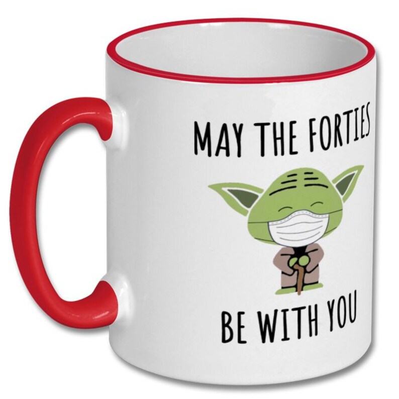 May include: White ceramic coffee mug with a red rim and handle. The mug features a green cartoon character wearing a face mask and the text "May the Forties Be With You".