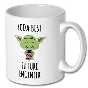 Könnte beinhalten: Weißer Keramikbecher mit großem Henkel. Der Becher zeigt ein Cartoon-Bild von Yoda mit dem Text "YODA BEST FUTURE ENGINEER" in Schwarz. Die Yoda-Figur ist grün mit großen Ohren und einem braunen Gewand.