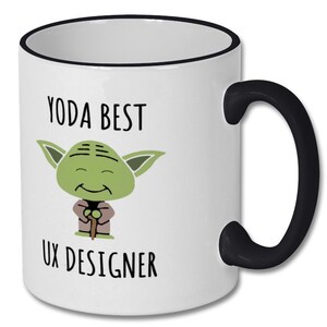 Może przedstawiać: Biały kubek ceramiczny z czarną obw&oacute;dką i uchwytem. Kubek przedstawia kresk&oacute;wkową postać Yody z Gwiezdnych Wojen, z tekstem "Yoda Best UX Designer".