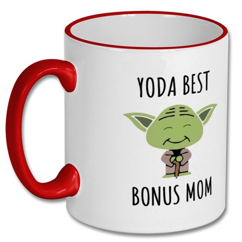 K&ouml;nnte beinhalten: Wei&szlig;er Keramikbecher mit rotem Henkel und Rand. Der Becher zeigt ein Cartoon-Bild von Yoda mit dem Text "YODA BEST BONUS MOM" in schwarzer Schrift. Ein lustiges Geschenk f&uuml;r eine Bonus-Mama.