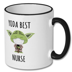 K&ouml;nnte beinhalten: Wei&szlig;e Keramiktasse mit schwarzem Rand und Henkel. Die Tasse zeigt ein Cartoon-Bild von Yoda mit einer Gesichtsmaske und dem Text "Yoda Best Nurse".