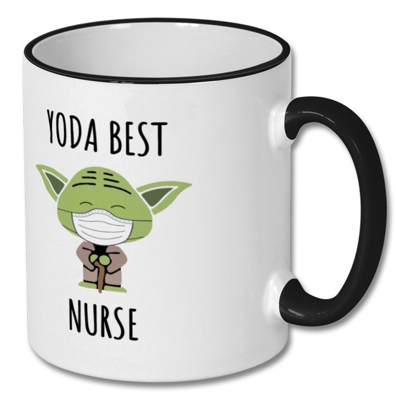 K&ouml;nnte beinhalten: Wei&szlig;e Keramiktasse mit schwarzem Rand und Henkel. Die Tasse zeigt ein Cartoon-Bild von Yoda mit einer Gesichtsmaske und dem Text "Yoda Best Nurse".