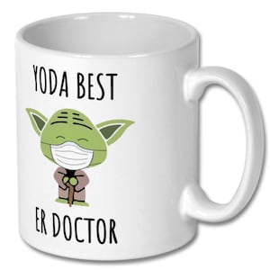 Może przedstawiać: Biały ceramiczny kubek do kawy z zieloną postacią Yody w maseczce i trzymającą laskę. Na kubku nadrukowany jest tekst "YODA BEST ER DOCTOR".