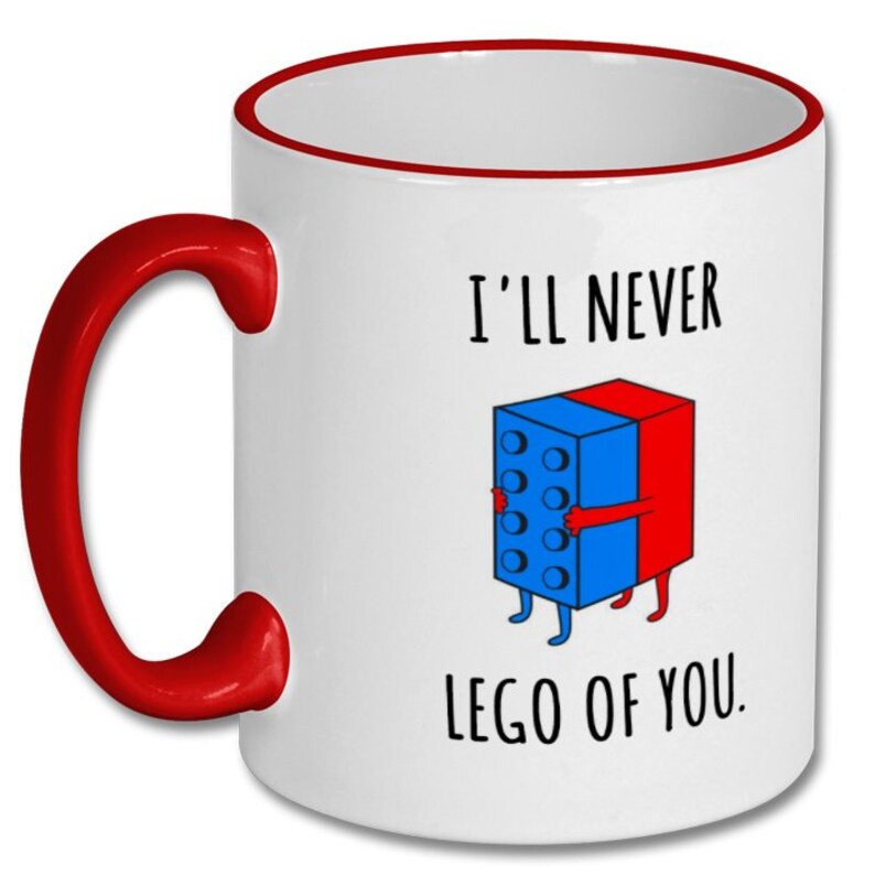 May include: White ceramic coffee mug with a red rim and handle. The mug has a blue and red Lego block illustration with the text "I'll never lego of you."