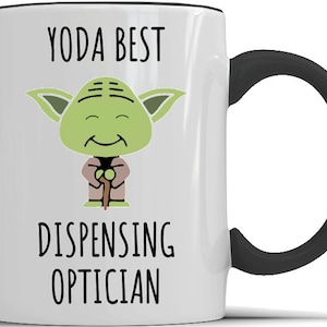 May include: White ceramic mug with a black handle. The mug has a cartoon image of Yoda from Star Wars with the text "YODA BEST DISPENSING OPTICIAN".