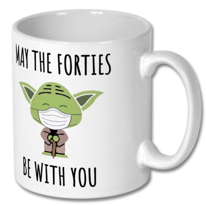May include: White ceramic mug with a green Yoda character wearing a face mask. The mug has the text "May the Forties Be With You" printed on it.