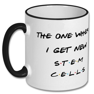 May include: White ceramic coffee mug with a black rim and handle. The mug features a black graphic that says "The One Where I Get New STEM CELLS" with colorful dots between the letters.
