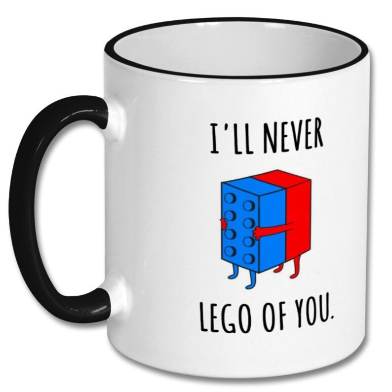 May include: White ceramic coffee mug with a black rim and handle. The mug features a cartoon illustration of two Lego blocks hugging each other. The text on the mug reads "I'll never lego of you."