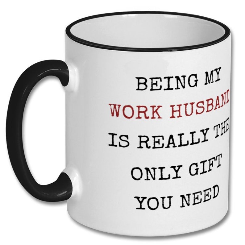 May include: White ceramic mug with a black handle and rim. The mug features the text "BEING MY WORK HUSBAND IS REALLY THE ONLY GIFT YOU NEED" in black and red lettering. A humorous gift idea.