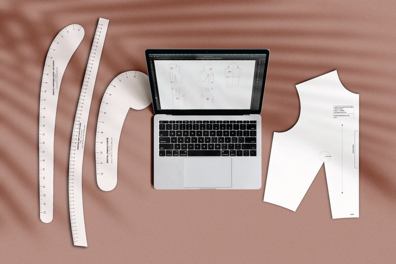 May include: A flat lay of a laptop computer, three white plastic French curve rulers, and a white paper pattern for sewing a garment. The laptop screen shows a digital drawing of a garment design.