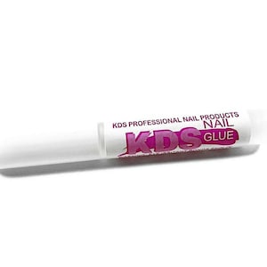 K&ouml;nnte beinhalten: Eine wei&szlig;e Tube KDS Professional Nail Products Nagelkleber. Die Tube hat eine wei&szlig;e Applikatorspitze und ein Etikett mit dem Markennamen in Lila und Wei&szlig;. Der Text auf dem Etikett warnt, dass das Produkt Augenreizungen verursacht und die Haut verklebt.