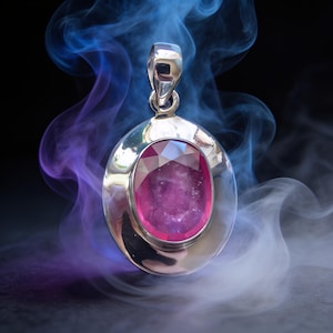 May include: A silver pendant featuring a large, oval-cut, deep pink gemstone set in a polished metal frame. The pendant has a sturdy bail at the top for attachment to a chain, surrounded by swirling wisps of blue and white smoke against a dark background.