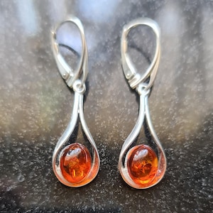 May include: A pair of silver teardrop earrings with amber-colored oval stones. The earrings have a lever back closure and a polished finish. The amber stones are a warm, translucent orange color.