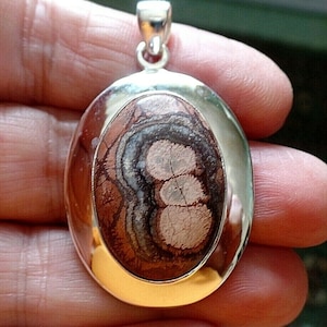 Peut inclure: Un pendentif en argent avec une pierre d'agate brune, blanche et noire sertie dans une bélière ovale. La pierre présente un motif tourbillonnant.