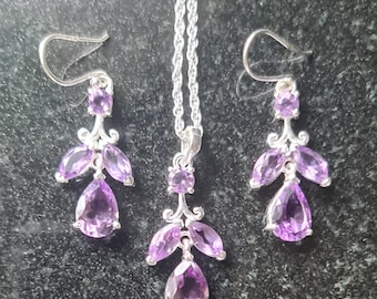 May include: A silver necklace and earrings set with a dangling design featuring multiple amethyst gemstones.