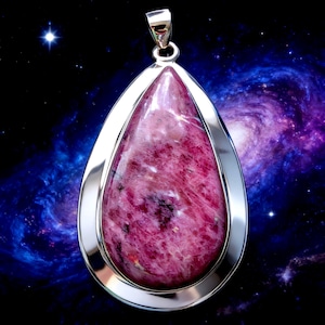 May include: A teardrop-shaped pendant with a polished, pink gemstone set in a silver frame. The gemstone has a marbled appearance with darker pink and black inclusions. The pendant hangs from a silver bail against a cosmic background.
