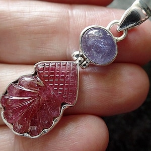 May include: A silver pendant with a carved pink gemstone and a round blue gemstone. The pendant is on a silver chain.