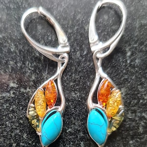 May include: Silver dangle earrings with turquoise and amber stones. The earrings have a leaf-like design with a turquoise stone at the bottom and amber stones in the center.
