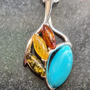 May include: Silver pendant necklace with a leaf-like design. The pendant features a large turquoise stone and several amber-colored stones in shades of yellow, orange, and green. The necklace chain is silver.
