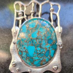 May include: A silver pendant with a large turquoise stone set in a geometric frame. The turquoise has a mottled pattern of blue and gold.