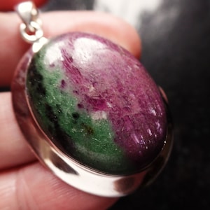 Peut inclure: Un pendentif en argent avec une pierre ovale verte et rose. La pierre précieuse a un motif marbré et est sertie dans une bélière en argent.