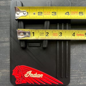Puede incluir: Objeto rectangular negro con un logotipo indio rojo y blanco. El objeto tiene crestas verticales y se mide con una cinta m&eacute;trica amarilla. El objeto mide aproximadamente 7,6 cm de ancho y 10,2 cm de largo.
