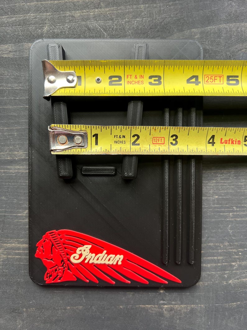Puede incluir: Objeto rectangular negro con un logotipo indio rojo y blanco. El objeto tiene crestas verticales y se mide con una cinta m&eacute;trica amarilla. El objeto mide aproximadamente 7,6 cm de ancho y 10,2 cm de largo.