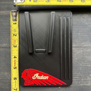 Puede incluir: Art&iacute;culo rectangular negro con crestas elevadas y el logotipo "Indian" rojo y blanco. El art&iacute;culo mide aproximadamente 12,7 cm de largo y 7,6 cm de ancho. Una cinta m&eacute;trica amarilla est&aacute; en el fondo.