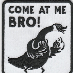 Könnte beinhalten: Weißer gestickter Aufnäher mit einer schwarzen Gans, die ihre Flügel ausgebreitet hat, und dem Text "COME AT ME BRO!" in Schwarz.