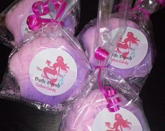 May include: Three shell-shaped bath bombs in clear plastic bags with pink ribbons. Each bath bomb has a gradient of light pink to purple and a circular label featuring a mermaid silhouette and the text The Soap Bar Bath Bomb Cotton Candy.