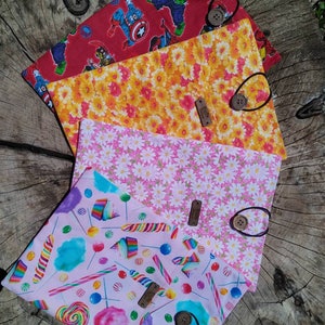May include: A stack of fabric pouches with various patterns. One pouch features Marvel comic book characters on a red background. Another has yellow and orange flowers. A third has white daisies on pink. The last has colorful candy on pink.