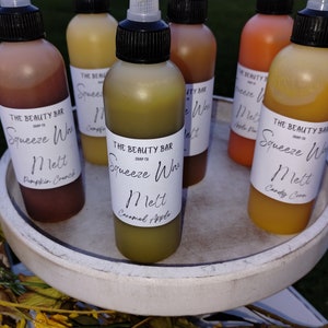 May include: Six small glass bottles with black caps and white labels. The labels say "The Beauty Bar" and "Squeeze Wax Melt" with different scents: Pumpkin Crunch, Caramel Apple, Apple Pie, Candy Corn, and two others.