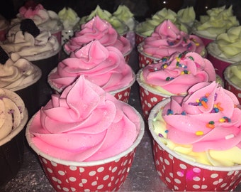 May include: A close-up of a variety of cupcakes with pink, white, and green frosting. The cupcakes are decorated with sprinkles and are in red and white polka dot cupcake liners.