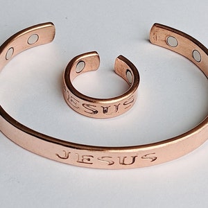 Könnte beinhalten: Ein Set aus zwei Kupferarmbändern mit der Gravur "JESUS". Das größere Armband hat magnetische Verschlüsse.