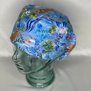 May include: A blue scrub hat with a mermaid and sea life pattern. The hat has a tie on the back.