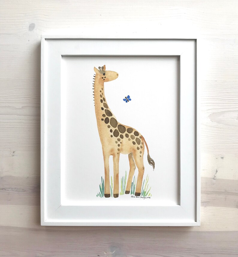 Pu&ograve; includere: Un dipinto ad acquerello di una giraffa in piedi in un campo di erba verde. La girafa &egrave; marrone con macchie marroni scure e ha un collo lungo. Una piccola farfalla blu vola vicino alla testa della girafa. Il dipinto &egrave; incorniciato in una cornice bianca.