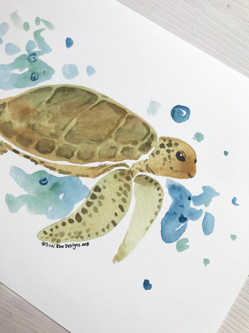 May include: Watercolour painting of a sea turtle swimming in blue water with green and blue watercolour splatter. The turtle is brown with a green shell and has a light brown face. The painting is signed "Suzi Blue Designs 2018".