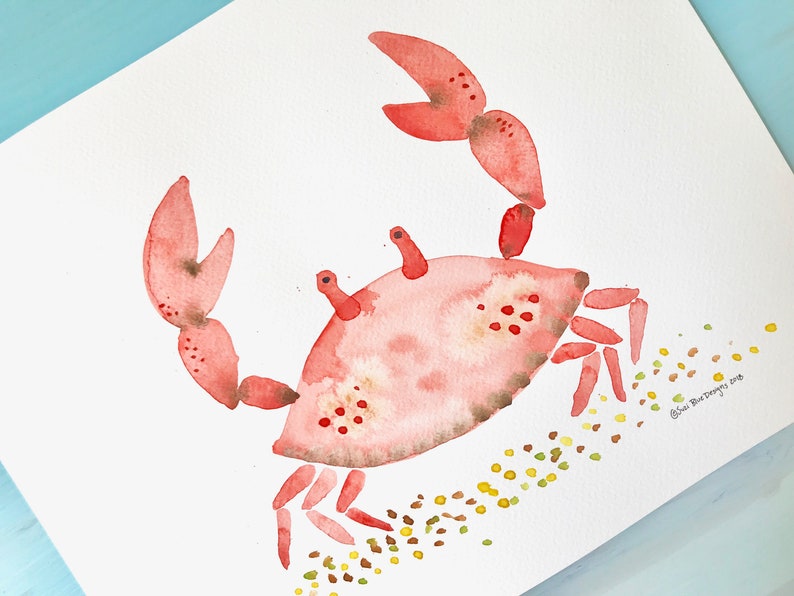 May include: Watercolor painting of a pink crab with yellow and brown dots on a white background. The crab is walking to the right and has its claws raised. The artist's signature is in the bottom right corner.