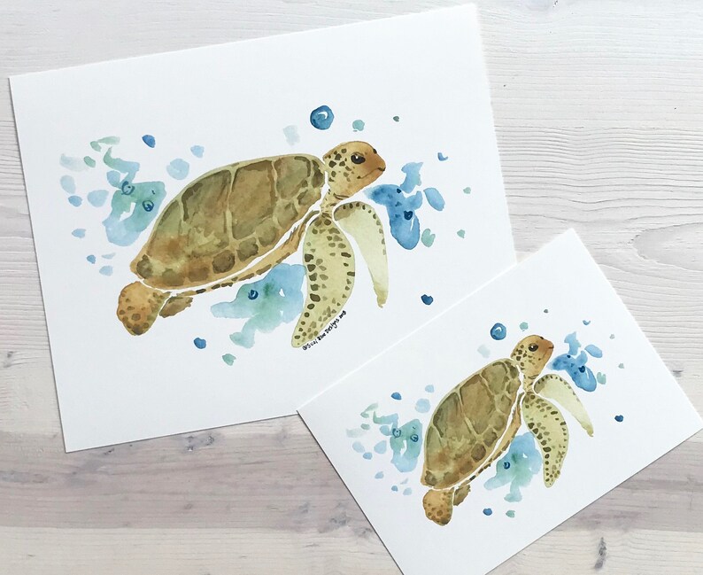 May include: Two watercolour paintings of sea turtles swimming in the ocean. The larger painting shows a turtle swimming to the right, while the smaller painting shows a turtle swimming to the left. Both paintings feature blue and green watercolour washes to represent the ocean.