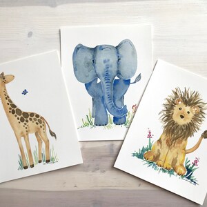 Pu&ograve; includere: Tre acquerelli di animali: una giraffa, un elefante e un leone. La giraffa &egrave; marrone e gialla con un collo lungo e macchie. L'elefante &egrave; blu con grandi orecchie e una proboscide. Il leone &egrave; marrone con una criniera gialla e una coda.