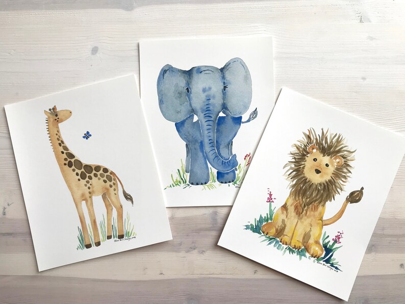 Pu&ograve; includere: Tre acquerelli di animali: una giraffa, un elefante e un leone. La giraffa &egrave; marrone e gialla con un collo lungo e macchie. L'elefante &egrave; blu con grandi orecchie e una proboscide. Il leone &egrave; marrone con una criniera gialla e una coda.